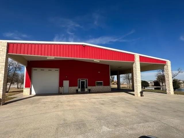 Red metal barndominium with stone pillars and concrete apron