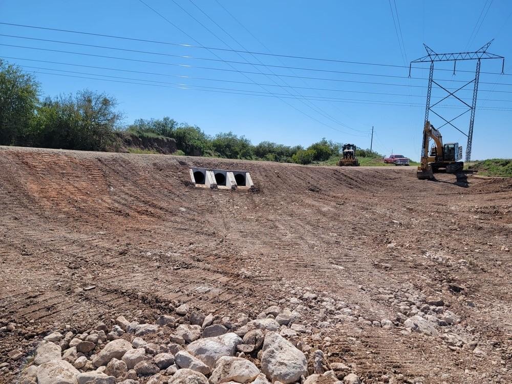 Drainage culvert installation with grading and excavator on civil construction site