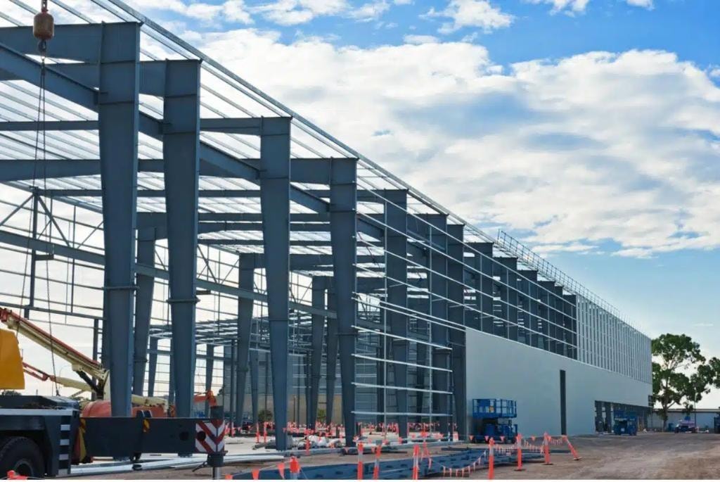 Steel framework construction of large commercial warehouse with crane and equipment on site